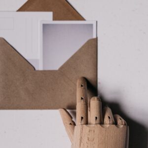 A wooden mannequin hand holds a brown envelope containing blank postcards.