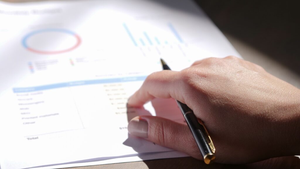 A close-up view of a hand holding a pen and examining financial charts on paper.