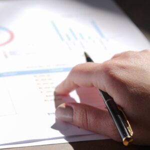 A close-up view of a hand holding a pen and examining financial charts on paper.