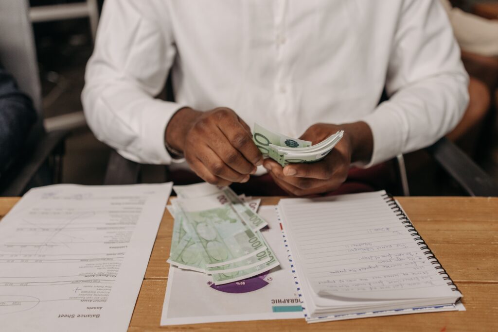 African businessman counting euro bills at a desk with documents and a notebook, highlighting finance theme.