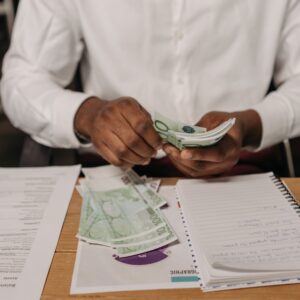 African businessman counting euro bills at a desk with documents and a notebook, highlighting finance theme.
